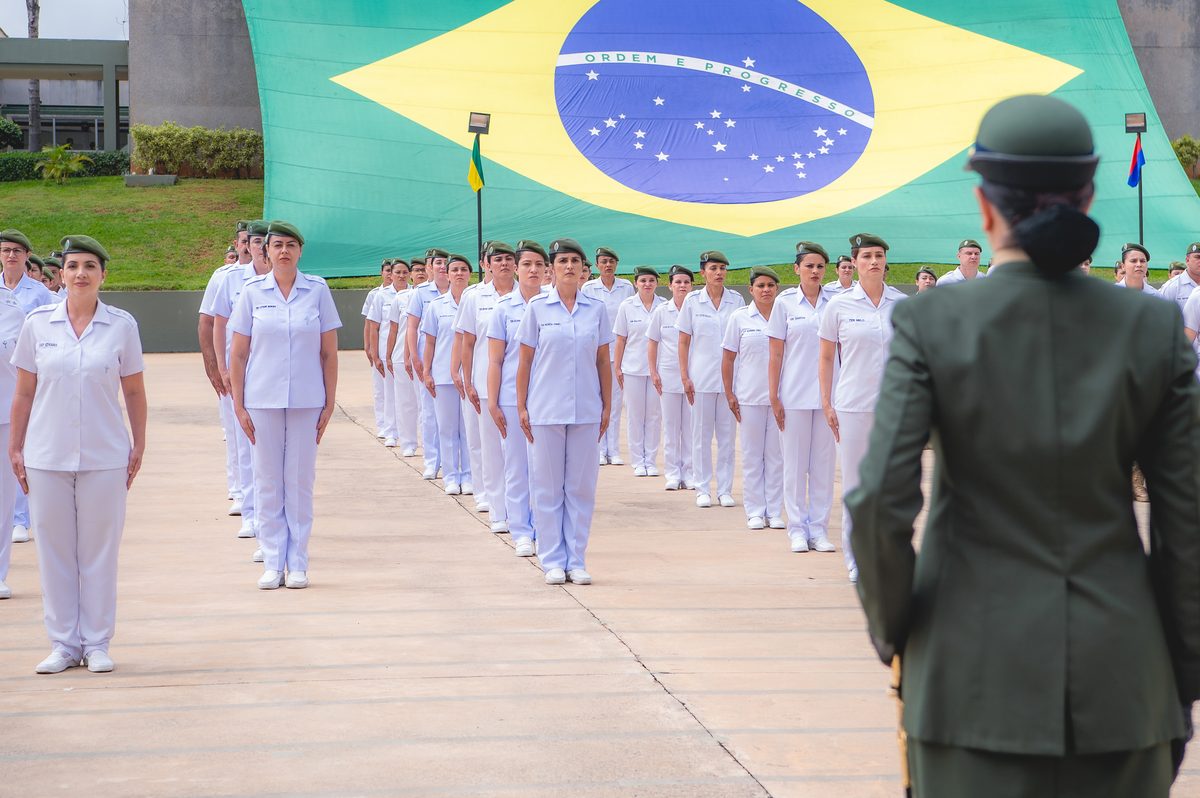Formação militar em frente a uma grande bandeira do Brasil