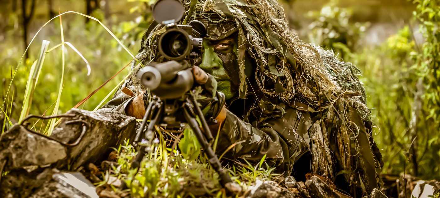 Militar camuflado em posição tática, representando o rigor e a precisão da vivência militar